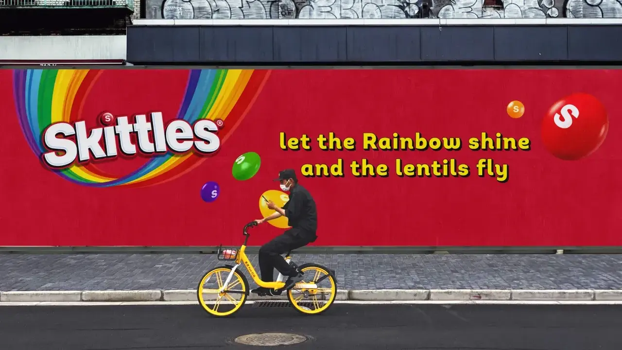 Skittles reklama: mężczyzna na rowerze pod tęczowym logo, latające cukierki. "Niech tęcza świeci, a soczewki latają".