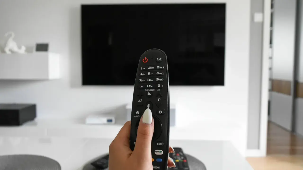 Dłoń trzymająca pilot do telewizora, gotowa do włączenia znanych utworów w reklamach.