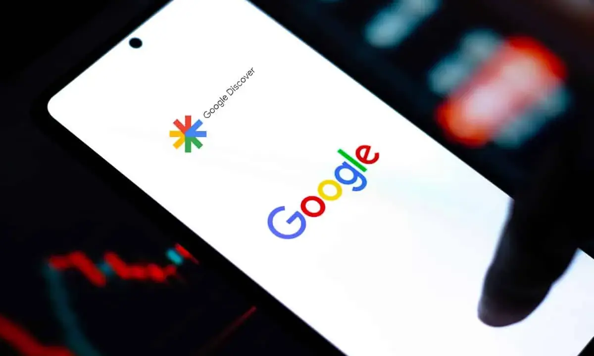 Ekran smartfona z logo Google i napisem Google Discover. W tle wykresy finansowe.