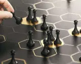 Dłoń kładzie pionka na heksagonalnej planszy. Strategia, jak w grze, kluczem do sukcesu w **guerrilla marketing**.