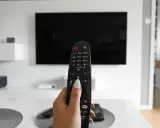 Dłoń trzymająca pilot do telewizora, gotowa do włączenia znanych utworów w reklamach.