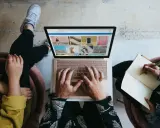 Zespół marketingu realizuje zadania: jedna osoba pisze na laptopie, druga notuje w zeszycie.
