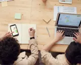 Dwie osoby analizują dane na laptopie i telefonie. Jedna pisze notatki, druga pracuje przy klawiaturze. To przykład pracy zespołowej, gdzie amp co to jest kluczowe dla sukcesu.
