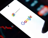 Ekran smartfona z logo Google i napisem Google Discover. W tle wykresy finansowe.