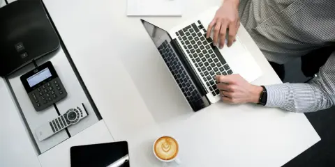 Biurko z laptopem, kawą i telefonem Cisco. Czy to jest CPL? Tak, to miejsce pracy.