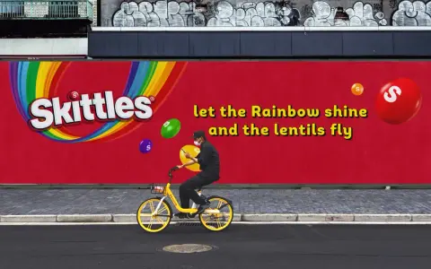 Skittles reklama: mężczyzna na rowerze pod tęczowym logo, latające cukierki. "Niech tęcza świeci, a soczewki latają".