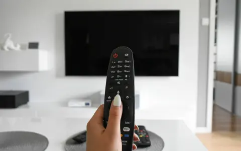 Dłoń trzymająca pilot do telewizora, gotowa do włączenia znanych utworów w reklamach.