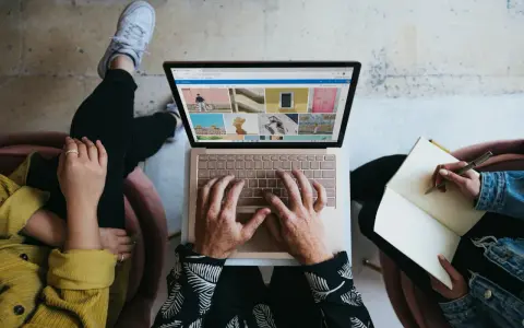 Zespół marketingu realizuje zadania: jedna osoba pisze na laptopie, druga notuje w zeszycie.