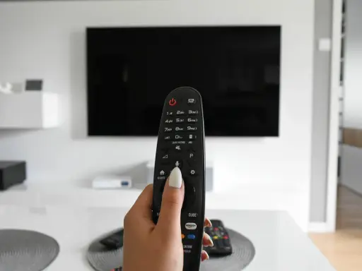 Dłoń trzymająca pilot do telewizora, gotowa do włączenia znanych utworów w reklamach.