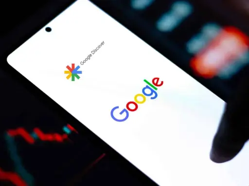 Ekran smartfona z logo Google i napisem Google Discover. W tle wykresy finansowe.