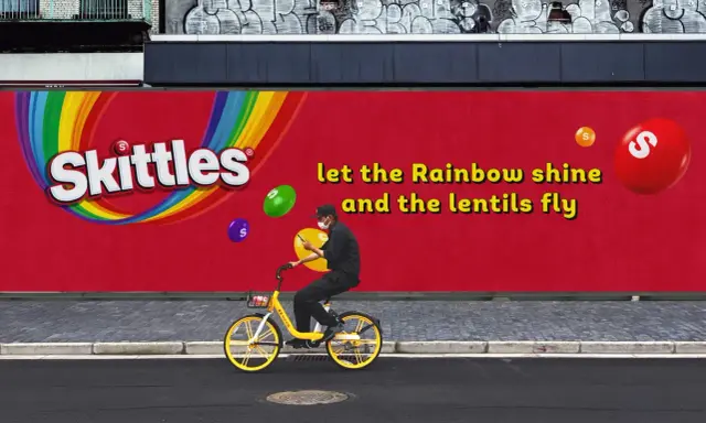 Skittles reklama: mężczyzna na rowerze pod tęczowym logo, latające cukierki. "Niech tęcza świeci, a soczewki latają".