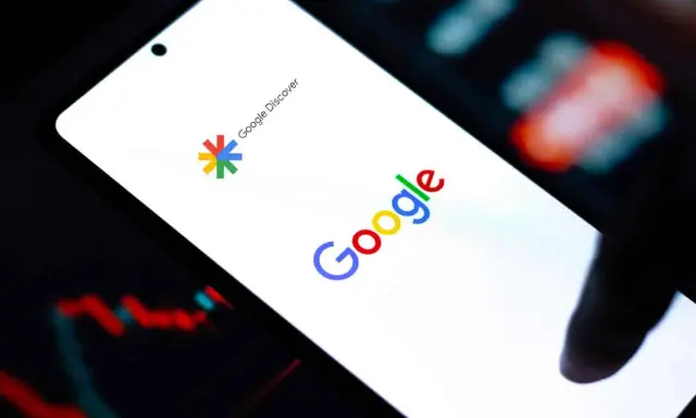 Ekran smartfona z logo Google i napisem Google Discover. W tle wykresy finansowe.